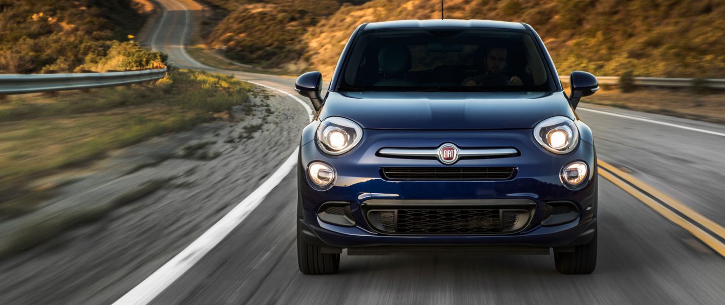 A three-quarter side view of a red 2020 Fiat 500X Sport parked on a cobblestone road.