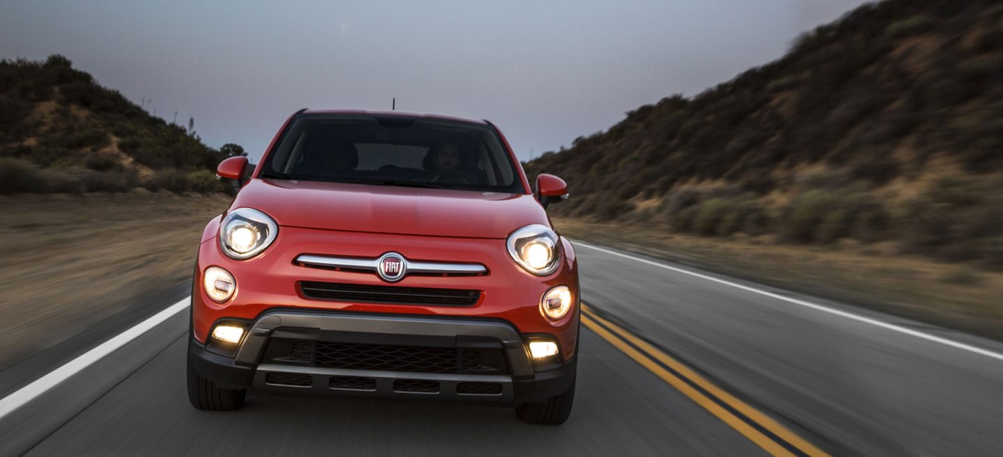 Three-quarter side view of a red 2020 Fiat 500X being driven on a downtown street at night.